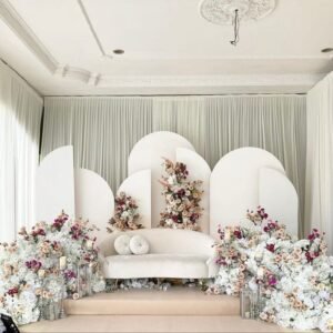 كوشة زفاف مهيبة تتوسط القاعة محاطة بكراسٍ بيضاء مُزينة بربطات زهرية، كل شيء يعكس أجواء الاحتفال والبهجة